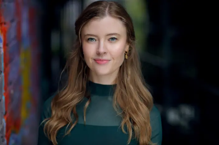 Portrait of voice actress Jennifer English with long wavy brown hair wearing a dark green top
