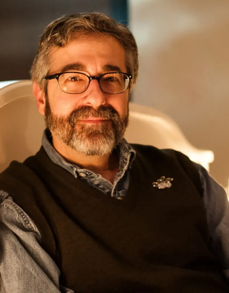 Portrait of game developer Warren Spector wearing glasses and a black sweater vest