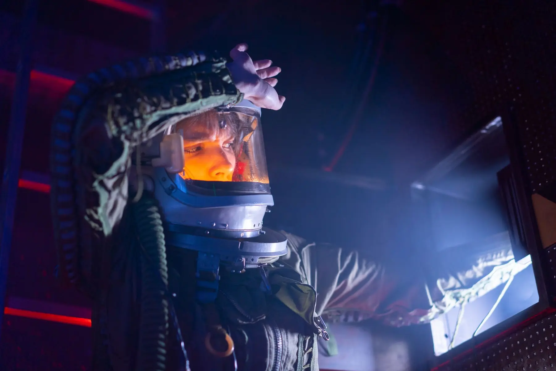 A person wearing a sci-fi space helmet and suit in a dark, neon-lit futuristic interior