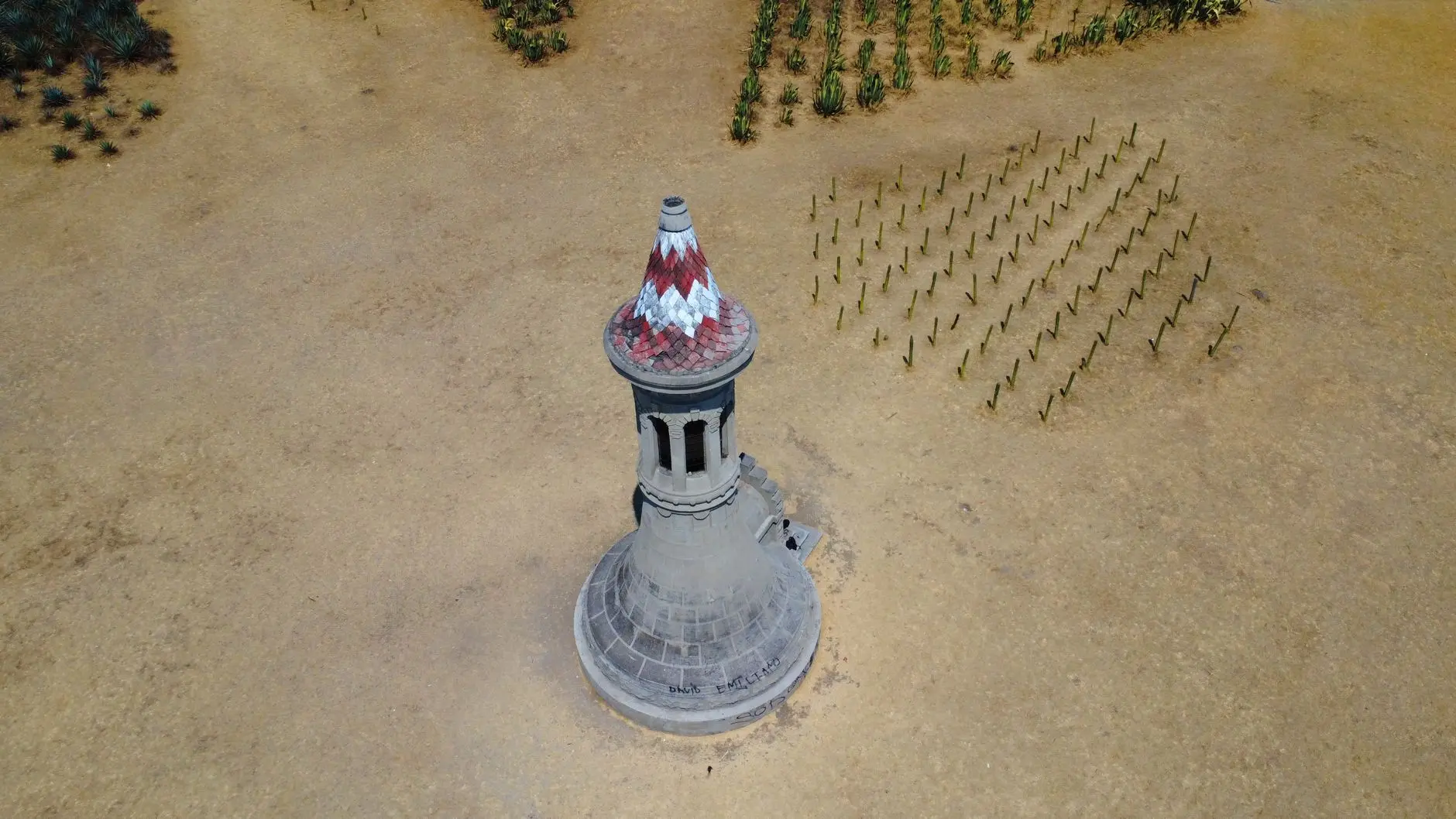 A high-angle view of a stone tower with a red-and-white tiled roof in a sandy landscape from Civilization VII.