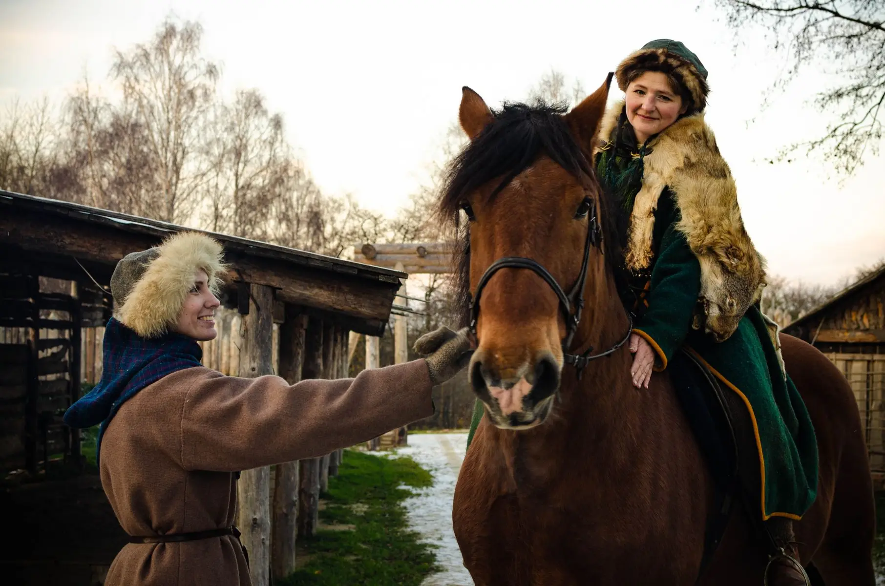 Two people in medieval-style clothing with a brown horse in a rustic outdoor setting