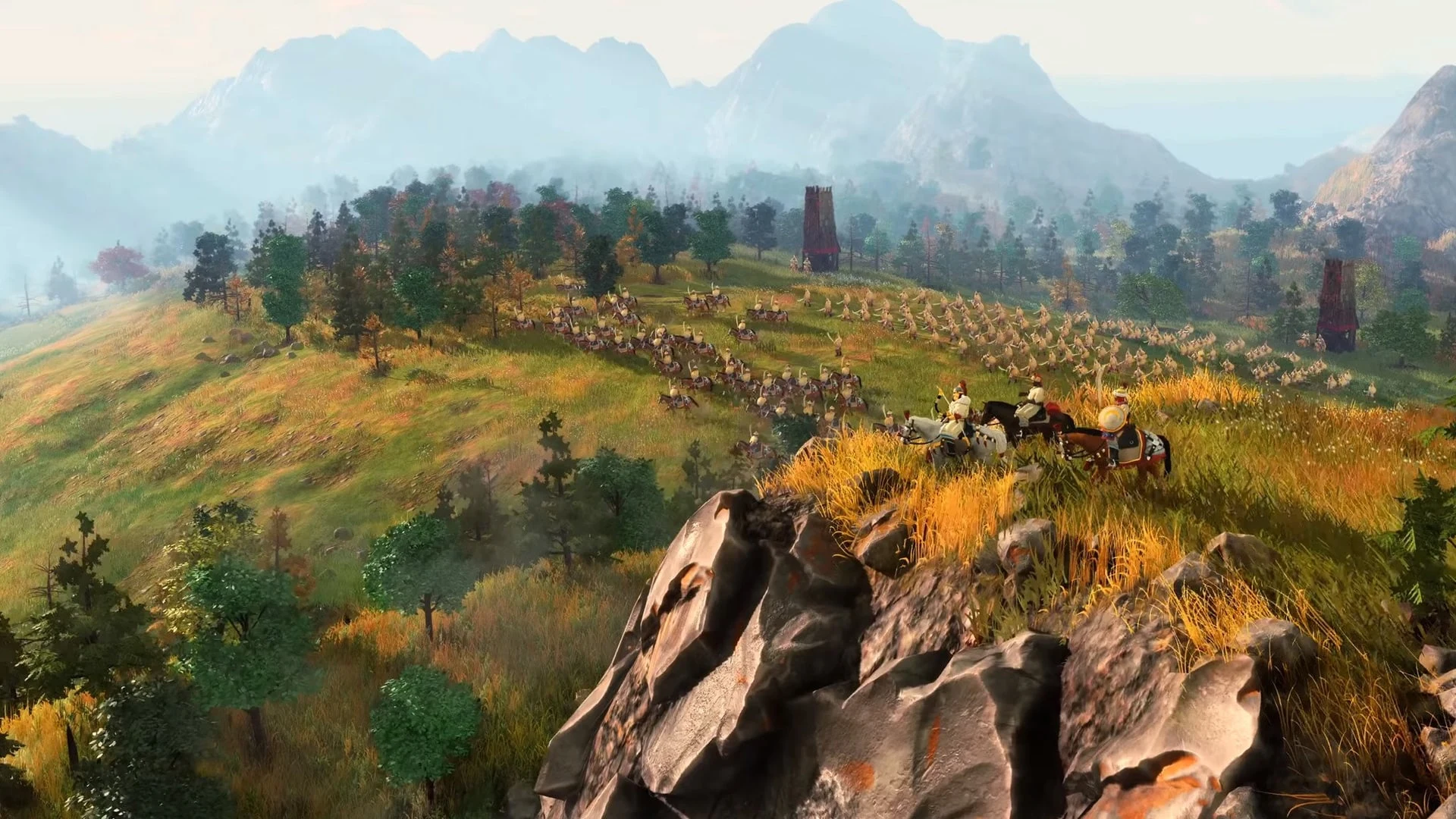 Kadr z rozgrywki Age of Empires IV przedstawiający armię kawalerii na zielonych wzgórzach przed górami.