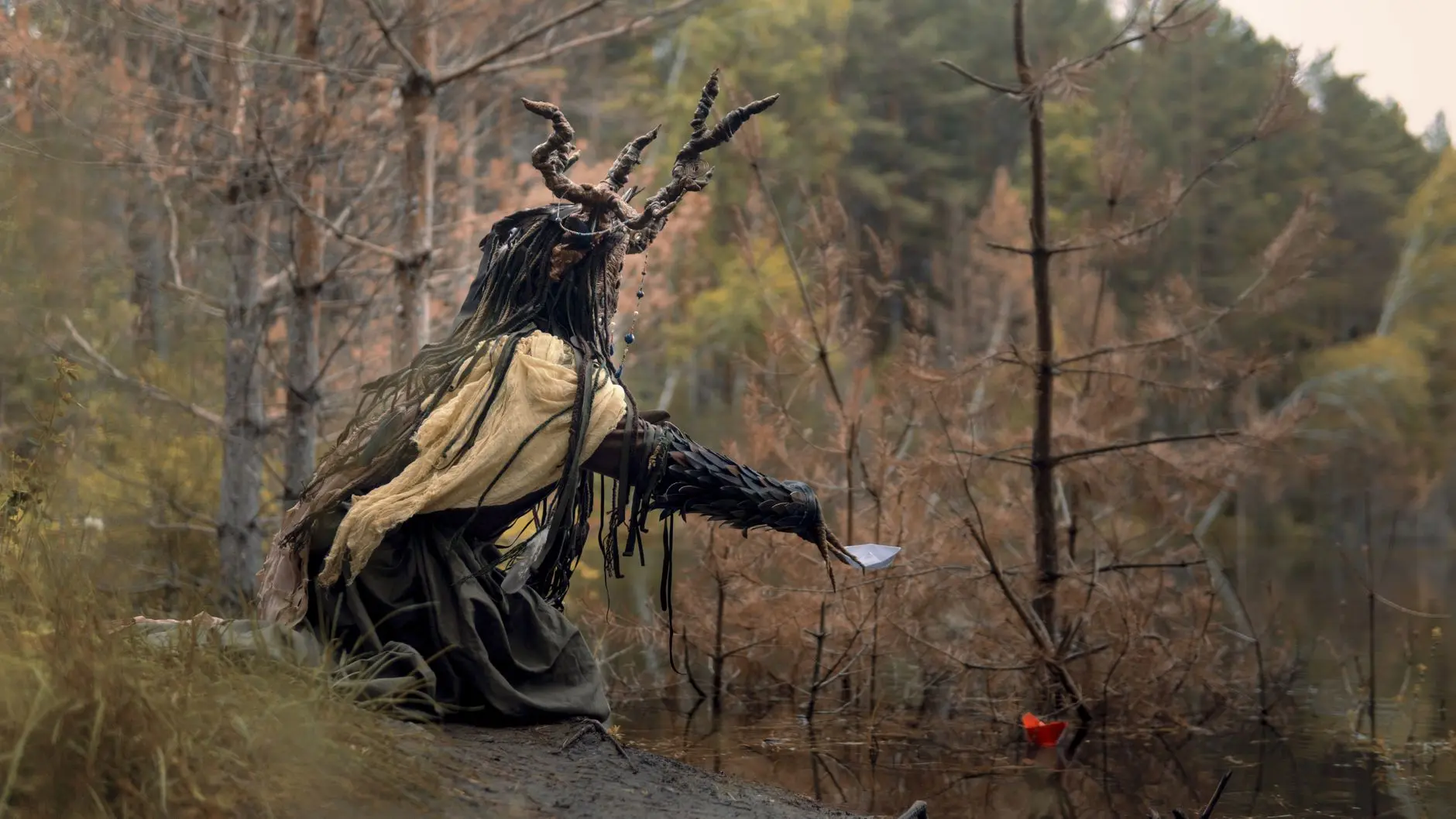 A character with branch-like antlers and ragged clothing standing by a swamp in Withering Realms